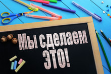 The Text We Can Do It (on Russian) On A Black Chalkboard On The Table With School Accessories (pens, Pencils, Brushes)