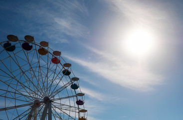 Ferris wheel on blue sky background and sun. In the amusement Park. The weekend