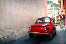 Red Old Well-preserved Vintage Italian Classic Car Parked In A Small Alley In An Italian Sicilian City With A Large Empty Stone Wall In The Left Side Of The Frame.