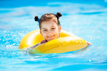 Little girl in the pool with a yellow life buoy