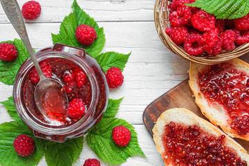 Raspberry jam and sandwiches with fresh raspberries in wicker bowl