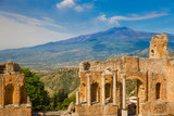 Fototapeta  - Panoramic view of beautiful town of Taormina with its greek amphitheatre and Etna volcano background, Sicily island, Italy