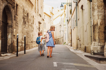 Group of two kids walking on the streets of old european town, wearing backpacks. Travel with children. Back view