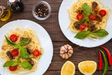 Fototapeta Tulipany - Two dishes of Spaghetti with beef meat slices, cherry tomatoes and basil leaves on white plate. Rustic wooden table  on background. Ideas for restaurant menu. 
