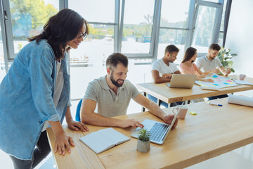 Wall Mural - Handsome pleasant man showing a laptop to his colleague