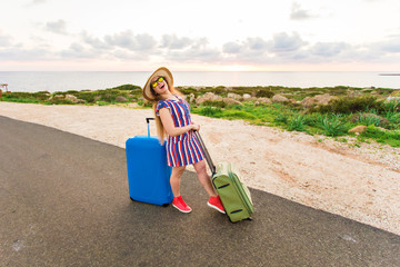 Happy cheerful traveler woman standing with suitcases on the road and smiling. Concept of travel, holidays, journey, trip