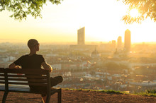 A Man On A Bench In A Park, Relaxing And  Enjoying The Summer Sunrise Over A City. Lyon, France.