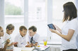 © kuzmichstudio - Beautiful children, the students and teacher together in a classroom at the school receive education with tablets happy