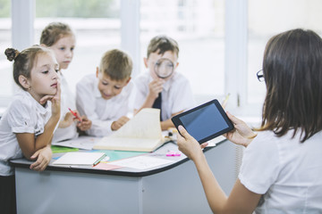 Beautiful children, the students and teacher together in a classroom at the school receive education with tablets happy