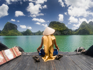 Wall Mural - man wearing a Vietnamese hat enjoying the magnifiecent sight of Ha Long bay limestone rocks on a beautiful sunny day during a boat cruise, Vietnam