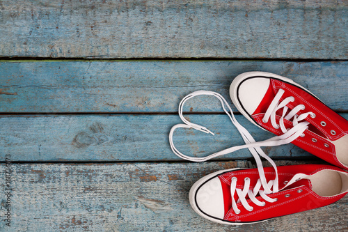 Photographie A pair of red retro sneakers on a blue wooden background, laces lined in a heart shape