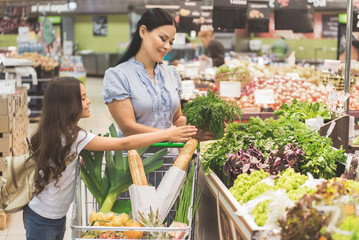 Outgoing child and cheerful mother buying dill