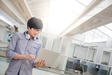 Young Asian business man dressed in casual style working with his laptop computer. Digital nomad in co working space, modern IT lifestyle with work life balance concept.