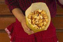 Popcorn. In The Background, The Hand Of A Child Holding Boxing Of Popcorn.