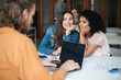 © Anton - Portrait of two smiling beautiful girls sitting in classroom and gossiping while young man working on his laptop. Two pretty girls sitting in office and dreamily looking aside