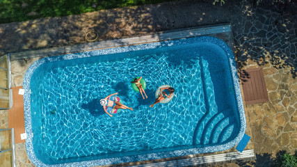 Wall Mural - Aerial top view of family in swimming pool from above, happy mother and kids swim on inflatable ring donuts and have fun in water on family vacation
