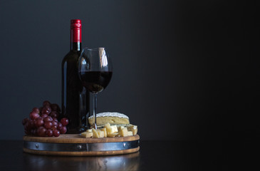 Bottle and glass with red wine near cheese composition on a wooden board