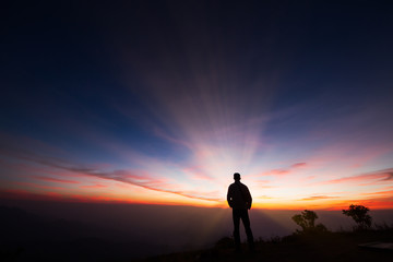 Silhouette of a man standing on the cliff looking at sunrise background, hope and following a dream concept