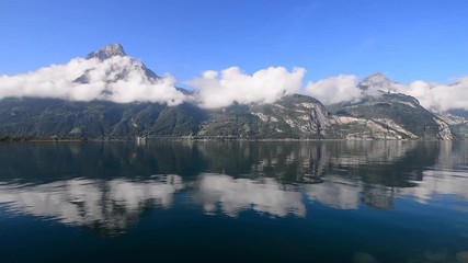 Sticker - Relaxed morning on the lake in the Alps. The tops of the mountains and white clouds are reflected in the surface of the water, a mirror.