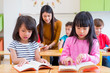 © weedezign - two Asian girl kid reading book in classroom and while teacher teach friends beside them,kindergarten education