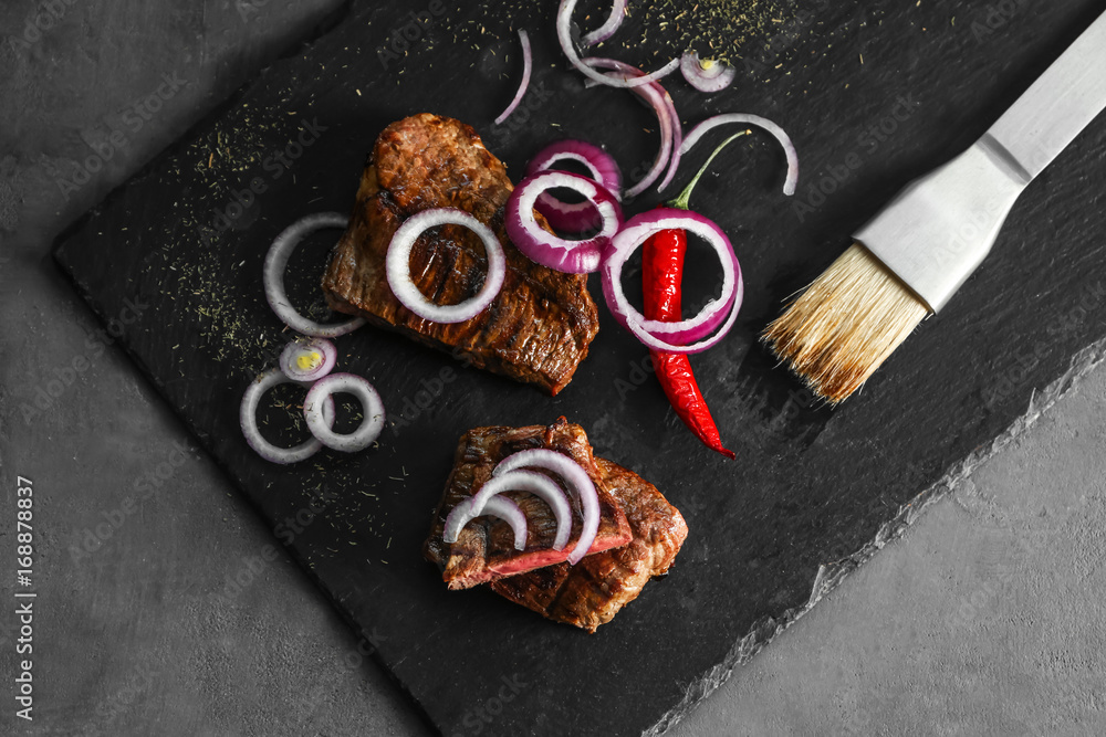 Delicious sliced meat with sauce and onion on slate plate