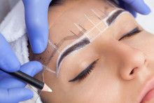 Permanent Make-up For Eyebrows Of Beautiful Woman With Thick Brows In Beauty Salon. Closeup Beautician Doing  Tattooing Eyebrow.