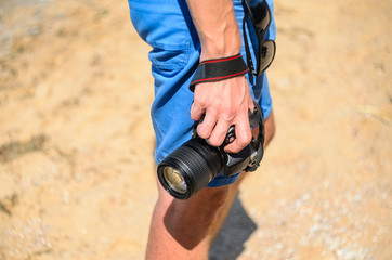 Dslr camera in the hands of a photographer on a sandy beach close up