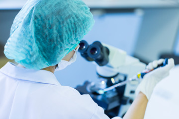 Rear view of Scientist holding pipette working a microscope at the laboratory