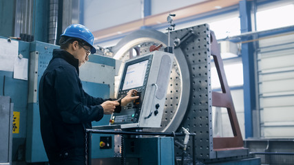 factory worker is programming a cnc milling machine with a tablet computer.