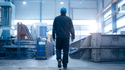 Factory worker in a hard hat is walking through industrial facilities.