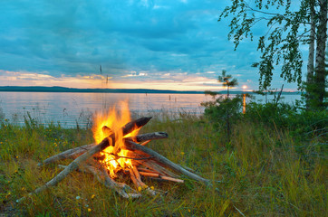 Wall Mural - Summer evening campfire by the river against the setting sun.