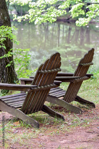 Empty Adirondack Chairs Along Wooded Shoreline Buy This Stock
