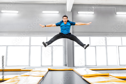 Fotografía A young fit happy man jumping and flying on trampoline in fitness gym