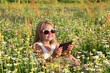 Śliczna uśmiechnięta dziewczynka bawi się tabletem wśród polnych kwiatów.