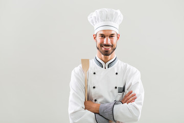 Wall Mural - Portrait of smiling chef holding wooden spoon on gray background.