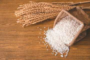 Close up of raw rice in burlap sack on wooden table.