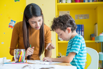 asian woman teacher teaching boy kid to paint color book on table in classroom,kindergarten educatio