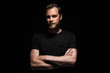 © _robbie_ - Portrait of a bearded man with an intense look standing in a dark room against a black background.