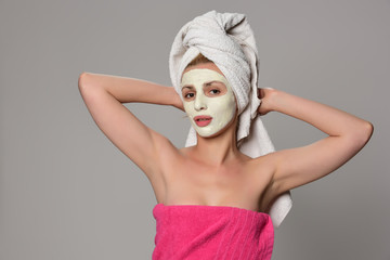 Beautiful female model with towel on her hear and white facial cosmetic mask on her face. Beauty cosmetic concept. Isolated on gray background.