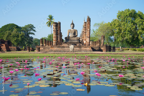 Fotografia Ruins of ancient Buddhist temple Wat Chana Songkram on the shore of a lake with pink lilies