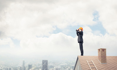 Engineer man standing on roof and looking in binoculars. Mixed m