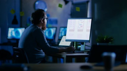 Male Mobile Application Developer Works with Graphics on His Personal Computer with Two Monitors. He Works Late at Night, in an Empty Office. Shot on RED EPIC-W 8K Helium Cinema Camera.
