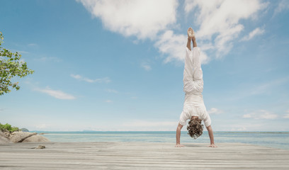 Young man doing yoga exercise - handstand, on a beautiful tropical beach