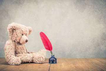 Wall Mural - Retro Teddy Bear toy with red quill pen in the inkwell front concrete wall background. Vintage instagram old style filtered photo