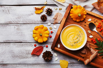 Wooden tray with hot autumn pumpkin soup decorated sesame seeds and thyme in white bowl on rustic vintage table top view. Cozy lifestyle shot for halloween menu.