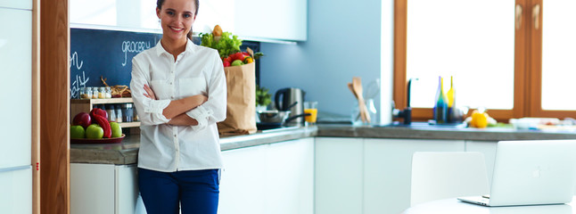 Portrait of young woman standing with arms crossed against kitchen background