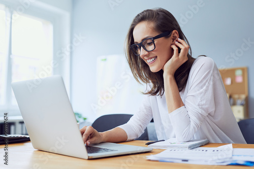 Plakat Portret veautiful rozochocony młody bizneswoman pracuje na laptopie i śmia się w ministerstwie spraw wewnętrznych