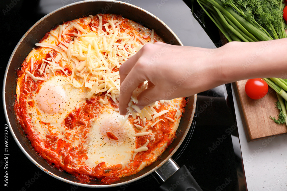 Woman pouring cheese on eggs in purgatory