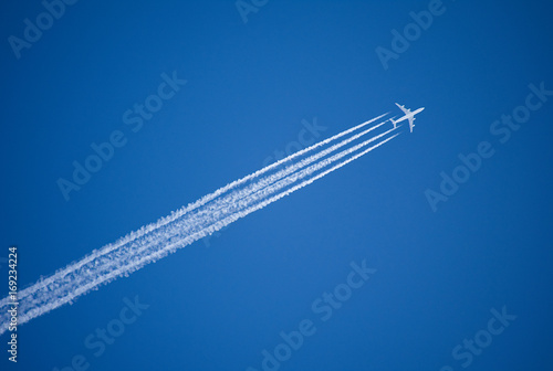 Fotografering  A jet plane flying overhead diagonally with condensation trail.
