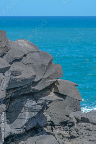 A Jagged Rock Formation With A Beautiful Blue Ocean Light Blue
